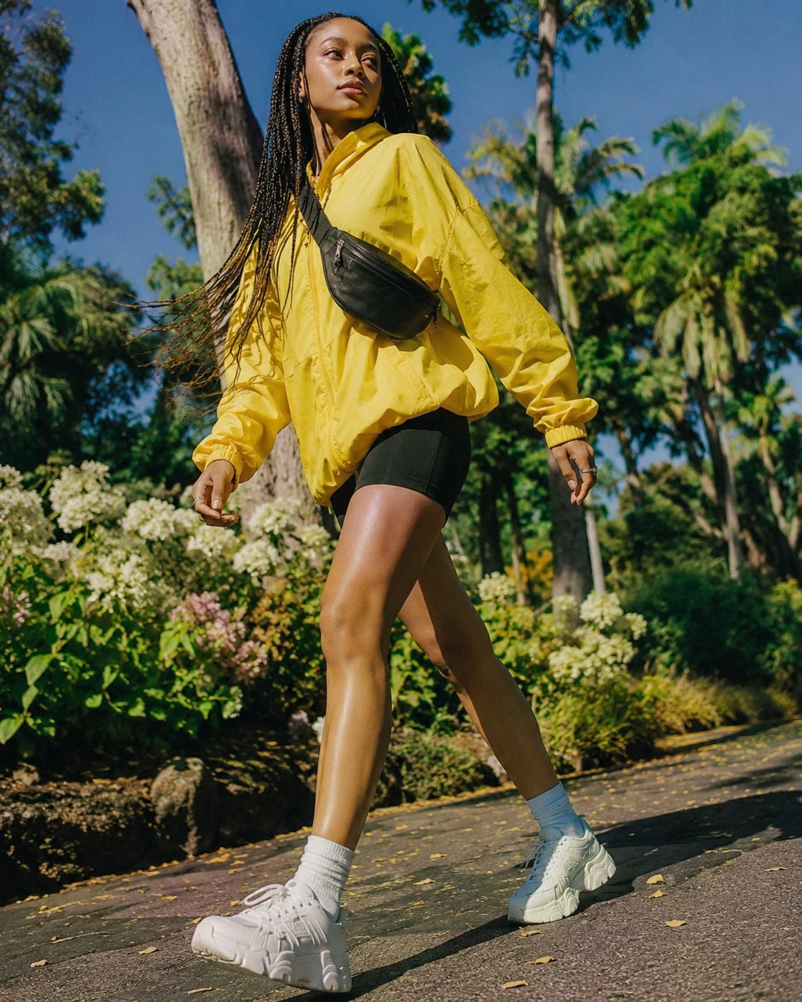 Woman walking in a yellow windbreaker and bike shorts, sporty 90s retro outfit inspiration in a park