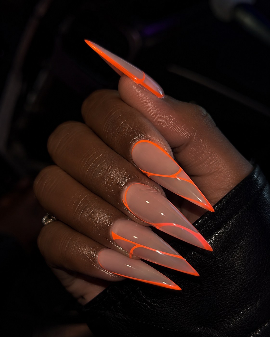 Neon orange negative-space outline on long stiletto nails against dark skin