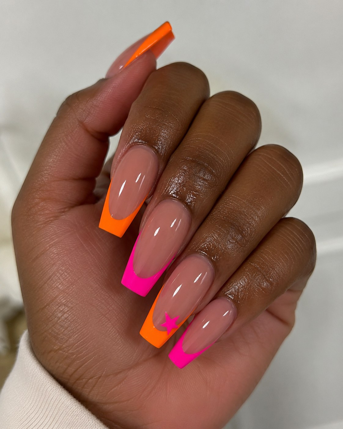 Neon orange and pink dual French tips over a nude base, a bold neon nails for dark skin look