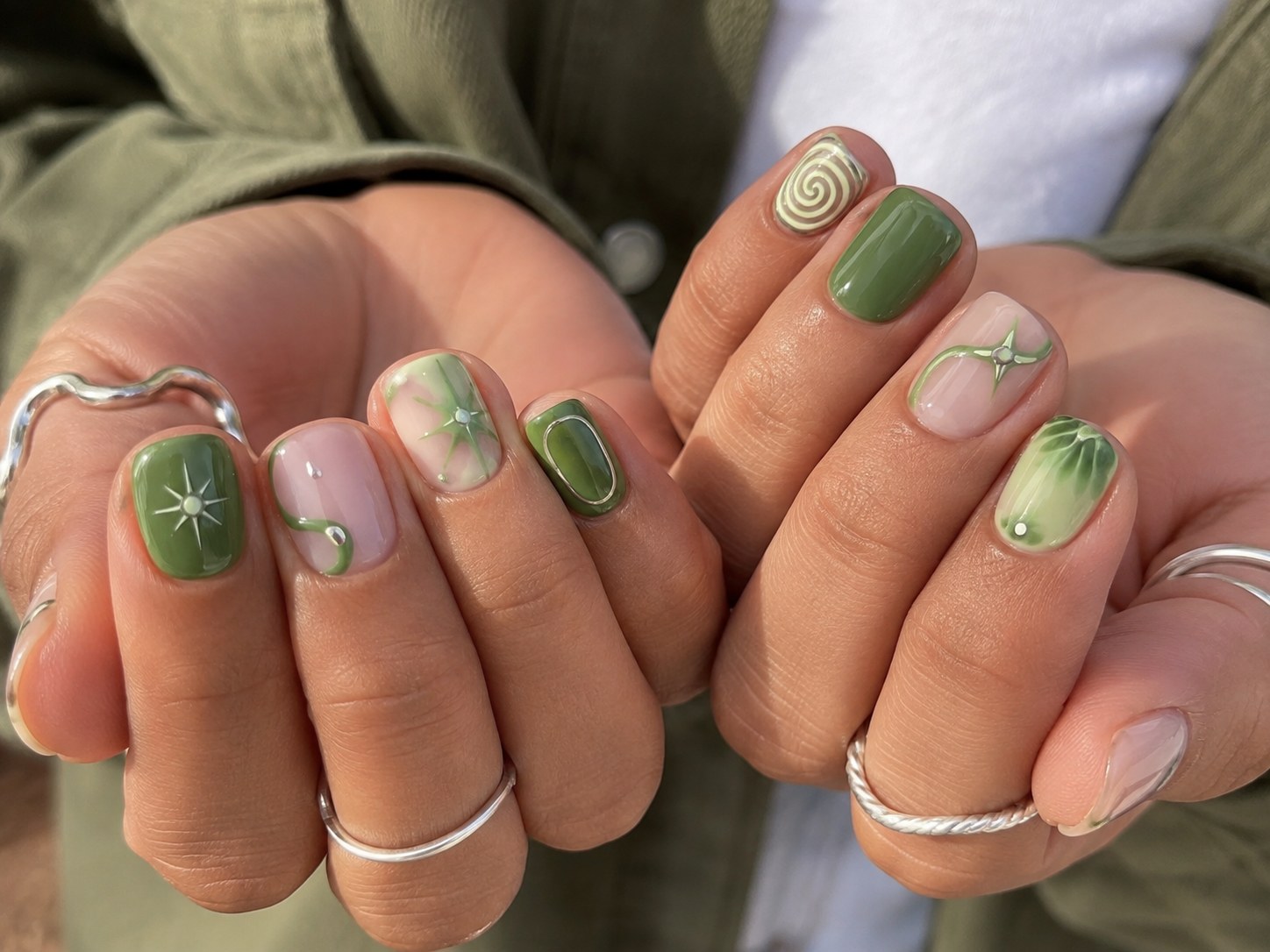 Short square nails in mixed sage and olive green with hand-painted spiral and star art