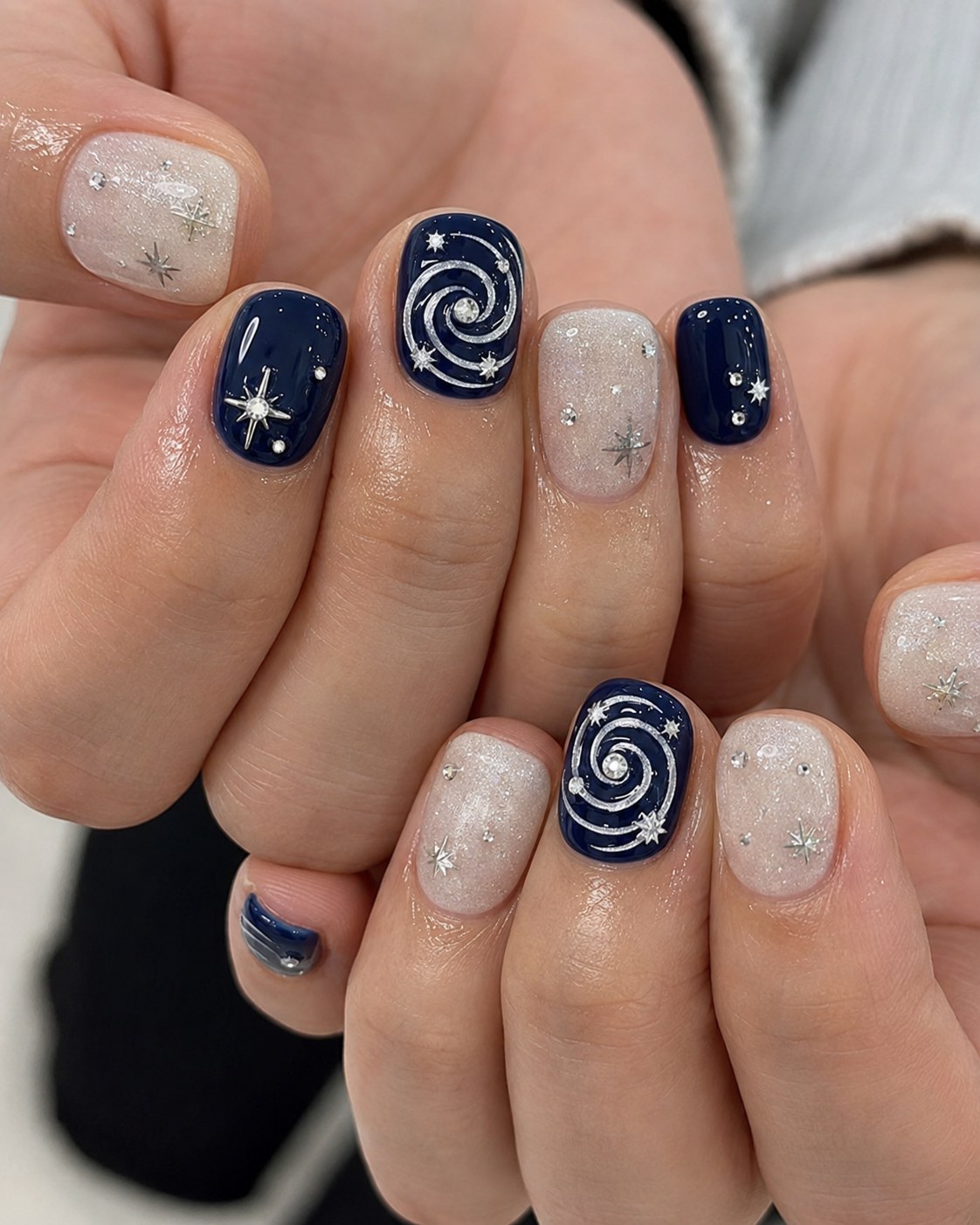 Short square nails alternating navy blue and glittery nude with white star and spiral art